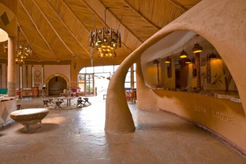 De gebeeldhouwde lemen balie van de receptie, met de naam van de Amboseli Sopa Lodge erin gegraveerd, onder een plafond van riet