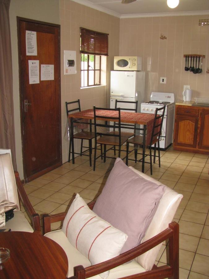 De kookhoek van een chalet, met eettafel, koelkast en magnetron, gezien vanuit een fauteuil met roze kussens