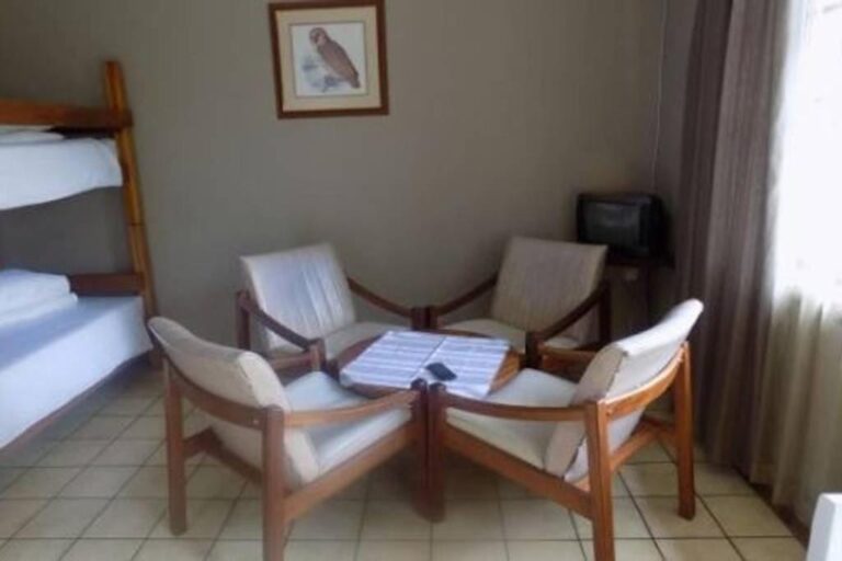 Vier fauteuils met witte kussens rond een salontafel, naast een stapelbed, onder een schilderij van een uil