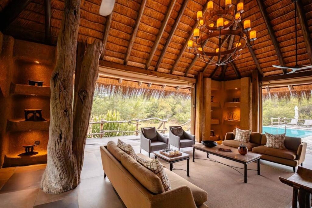De lounge van de Kapama River Lodge onder een hoog rieten dak, open naar een zwembad en de bush