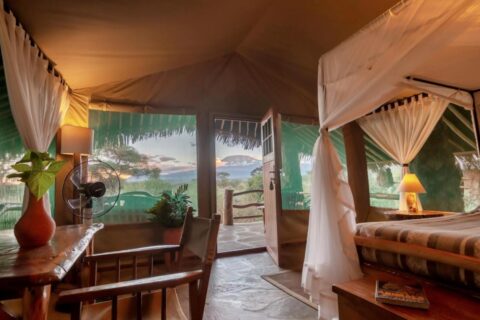 Een tent van het Kibo Safari Camp, open naar het terras, met de Kilimanjaro in de verte bij schemering