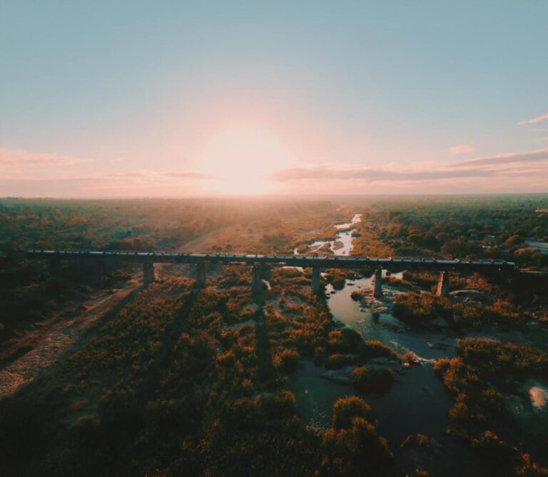 De trein van Kruger Shalati op de Selatibrug, van bovenaf gezien, boven de rivier en de bush, met de zon laag aan de horizon