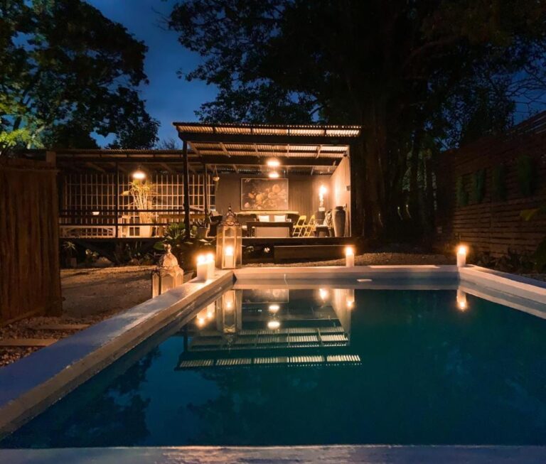 Het zwembad van Lush bij het vallen van de avond, verlicht met kaarsen, voor een overdekt terras met een golfplaten dak
