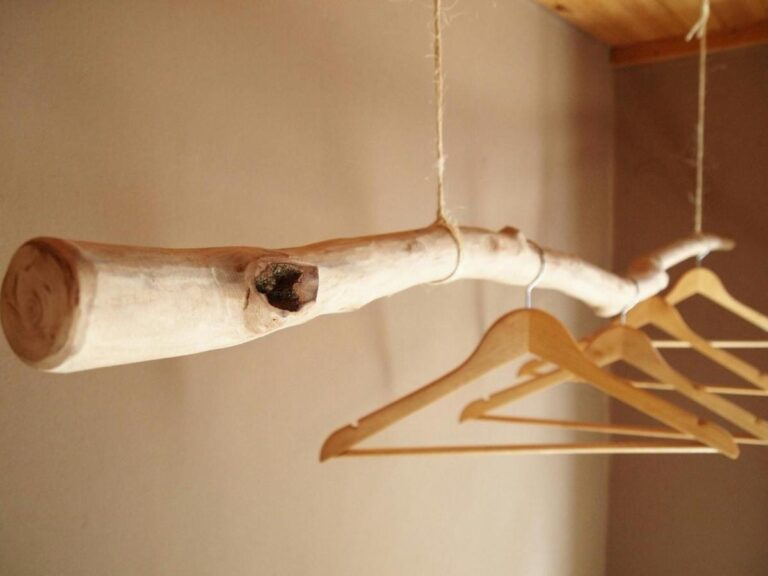 Houten kleerhangers aan een ontschorste tak, die met touwen aan het plafond hangt