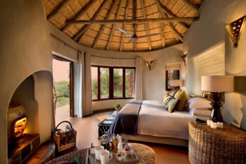 Een suite van de Madikwe Safari Lodge onder een rieten dak, met een tweepersoonsbed en een brandende open haard