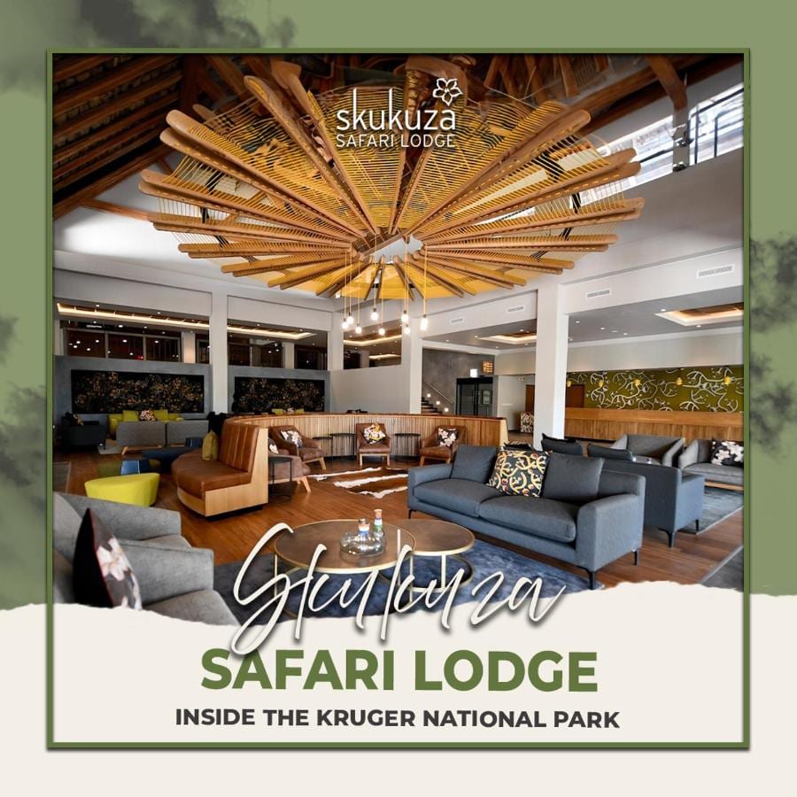 De lounge in de hal van de Skukuza Safari Lodge onder een stervormig plafond van houten latten, met de naam van de lodge eroverheen