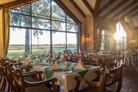 Het restaurant van het Sweetwaters Serena Camp, met gedekte tafels voor een grote glazen pui die uitkijkt op de vlakte