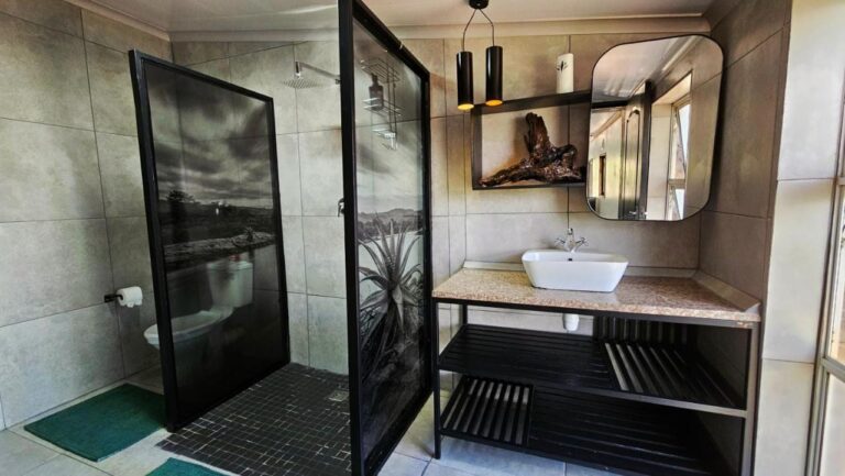 Een badkamer met een douche achter glazen wanden met zwart-witfoto's, en een opzetwastafel op een zwart meubel