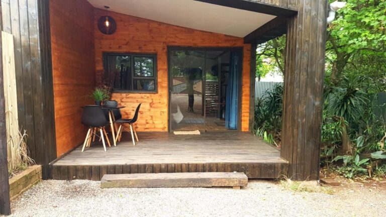Het houten terras van een chalet, met een tafel en twee zwarte stoelen voor een glazen schuifdeur
